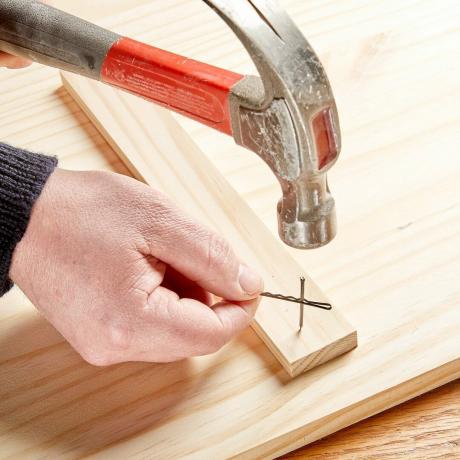 Verwenden Sie eine Mohnnadel, um einen Nagel zu halten, um ihn sicher in ein Stück Holz zu hämmern