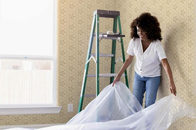 mujer pone un paño de plástico en una habitación con papel tapiz amarillo