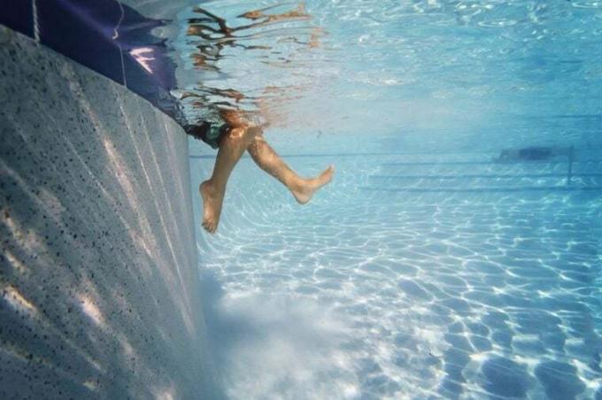 Gyermek lábai vízben a medence oldalán