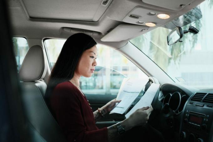 Kinesisk kvindelig leder arbejder i bil. Succesfuld asiatisk forretningskvinde, der bruger bærbar computer og kigger på papirarbejde.
