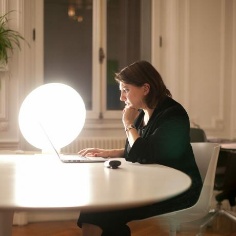 Sieviete sēž pie galda ar gaismas terapijas lampu