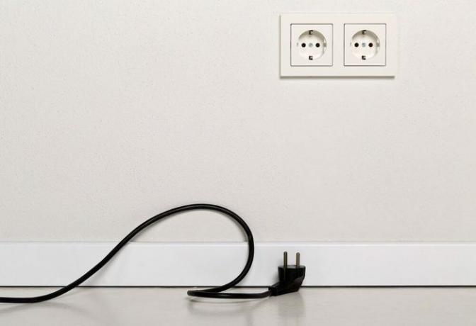 Kabel kabel listrik hitam dicabut dengan stopkontak Eropa di dinding plester putih dengan ruang fotokopi