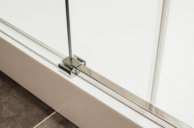Fixation métallique proche du bas de la porte coulissante en verre dans la cabine de douche vue de l'intérieur
