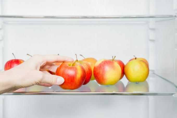 Kvinnens hånd tar vakkert, friskt, fargerikt eple fra kjøleskaphyllen på kjøkkenet. Sunn søt matkonsept. Ny start for sunn ernæring, slanking av kroppen, vekttap. Bryr seg om kroppen.