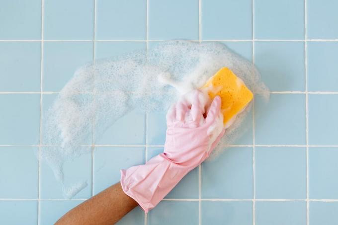 roze handschoen handreinigende blauwe badkamertegel met een zeepachtige gele spons