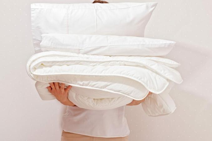 Женщина держит кучу постельных принадлежностей для сна