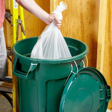 uomo che mette un sacco di spazzatura in un bidone della spazzatura verde con il coperchio attaccato con due fascette in un garage