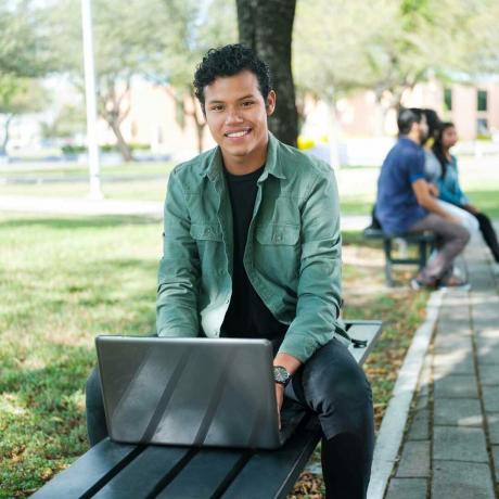 Opiskelija istuu ulkona kannettavan tietokoneen kanssa