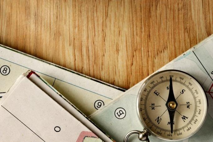 Zaprite instrument Vintage Compass na vrhu lesene mize z zloženimi zemljevidi, posnet v visokem kotu.