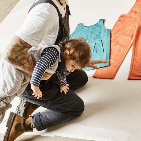 Bella Weinstein arrodillada y sosteniendo a su hijo mientras mira la ropa en el suelo