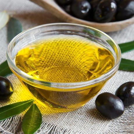 Olivenöl in einer Schüssel mit schwarzen Oliven an der Seite