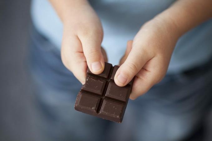Gebroken stuk donkere chocolade in de handen van het kind.