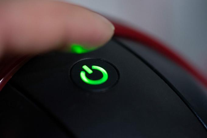 zblízka prst osoby dotýká zelené tlačítko napájení na spotřebiči
