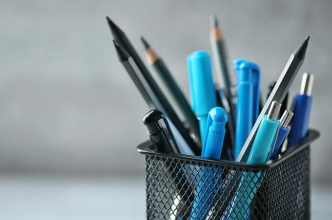 Pennen en potloden in metalen houder voor muurachtergrond