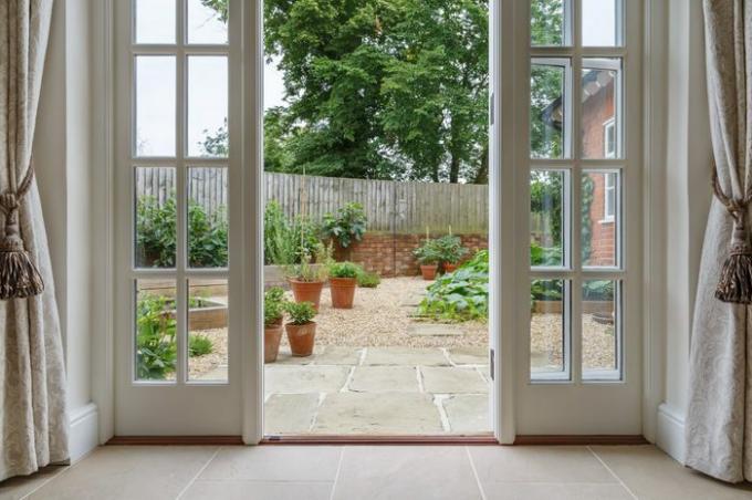 Vista del jardín desde el interior de la casa con puertas francesas que conducen a un patio con huerto