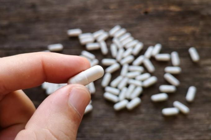 Hand met capsules pillen wit op houten achtergrond. Medische benodigdheden. Natuurlijke supplementen en vitamines