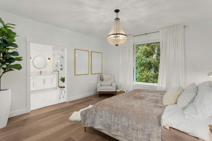 Hermoso dormitorio principal en nueva casa de lujo. Cuenta con una elegante lámpara colgante, pisos de madera noble y vista al baño principal en suite