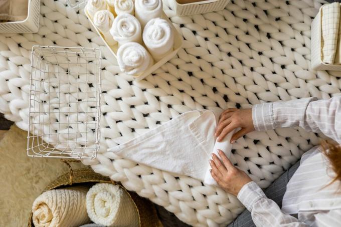 Pohľad zhora na ženské ruky úhľadne zložené biele čisté uteráky v krabici s použitím metódy usporiadania Marie Kondo