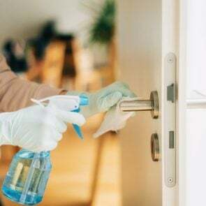 Donna che pulisce una maniglia della porta con uno spray disinfettante e una salvietta usa e getta