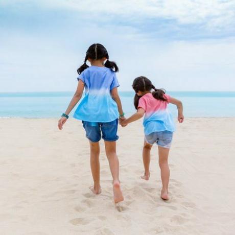 Dvě asijské sestry si hrají na pláži, dvě malé asijské dívky si užívají hraní a procházky po pláži ve dne, dvě asijské malé holčičky si užívají hraní na pěkné pláži