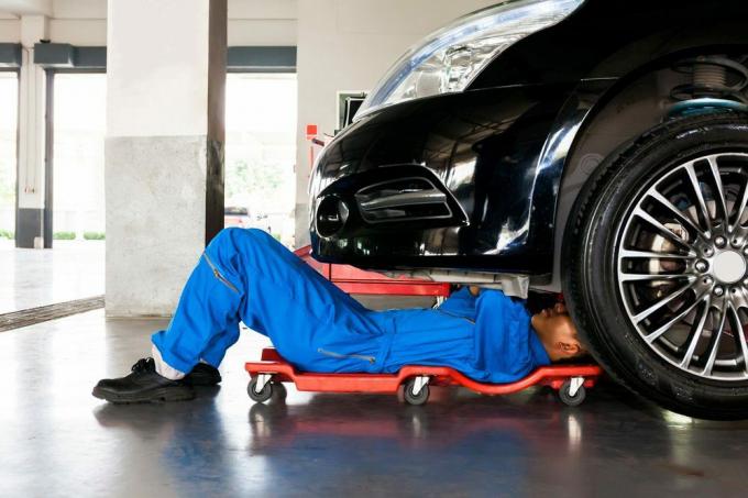 Механик в синей форме лежит и работает под автомобилем в гараже автосервиса