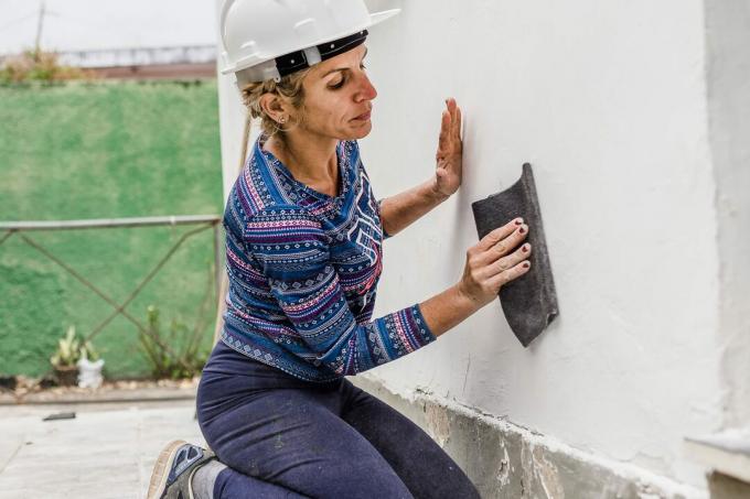 निर्माण श्रमिक महिला दीवार रेत रही है