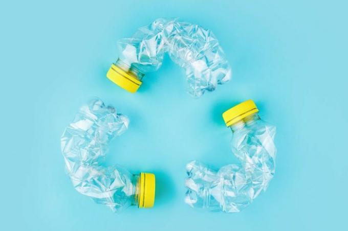 Trys sudužę plastikiniai buteliai mėlyname fone suformuoja pakartotinio važiavimo ženklą. Plastiko panaudojimo koncepcija. Patrauklus plakatas su ekologine problema. 