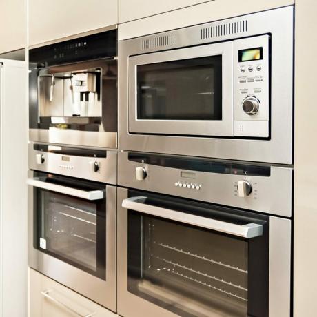 Luksuzno kuhinjsko posuđe, uključujući srebrnu pećnicu i hladnjak u kuhinji s drvenim podom, ormarići ostave su svijetlosmeđe boje i ugrađeni su oko štednjaka i hladnjaka.; Shutterstock ID 469237499