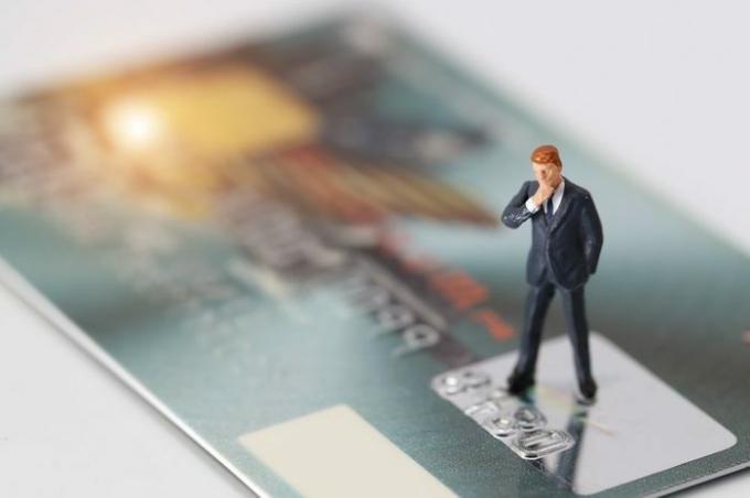 Miniatúrni ľudia: podnikateľ stojaci a premýšľajúci o niečom na kreditnej karte ako o online riešení platby a nákupu (koncept elektronického obchodu a nakupovania)