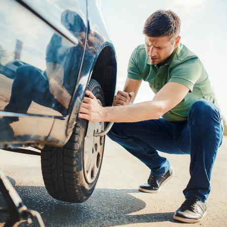 Hombre cambiando un neumático al costado de la carretera.