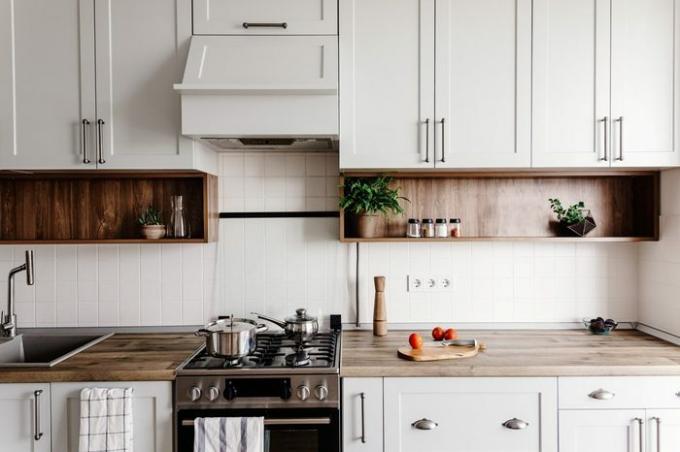 Gătit alimente în bucătăria modernă, cu mobilier în culoare gri și masă din lemn. Cuțit pe tăbliță de lemn cu legume, piper, condimente. Interior elegant de bucătărie în stil scandinav