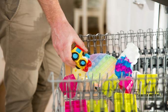 Un hombre poniendo juguetes sucios para niños en una máquina lavavajillas.