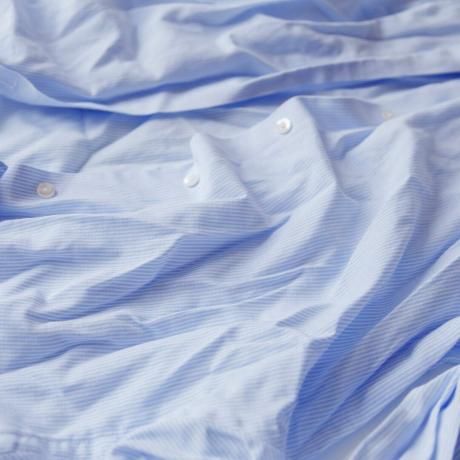 Blå bomullsrynket og krøllet skjorte på hvit. Vasket skjorte etter tørketrommel