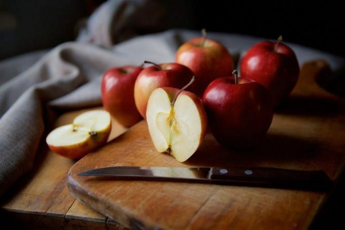 Яскраві соковиті червоні яблука лежать на старовинному сільському столі. Розріжте половину яблука на передньому плані.