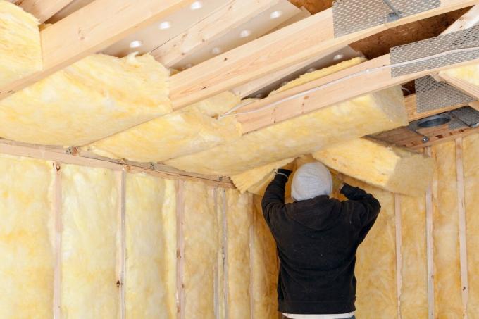 Trabajador instalando aislamiento de fibra de vidrio entre vigas de techo